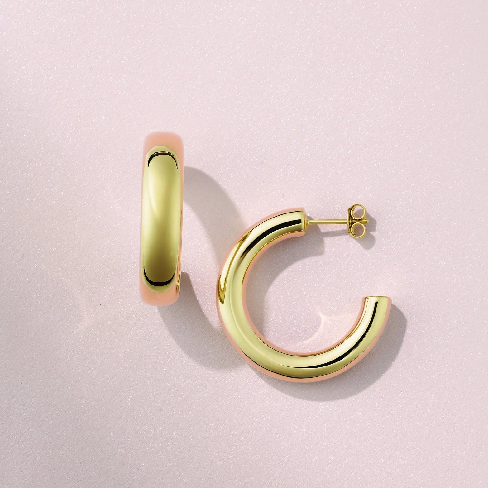 Gold hoop earrings on a light pink background